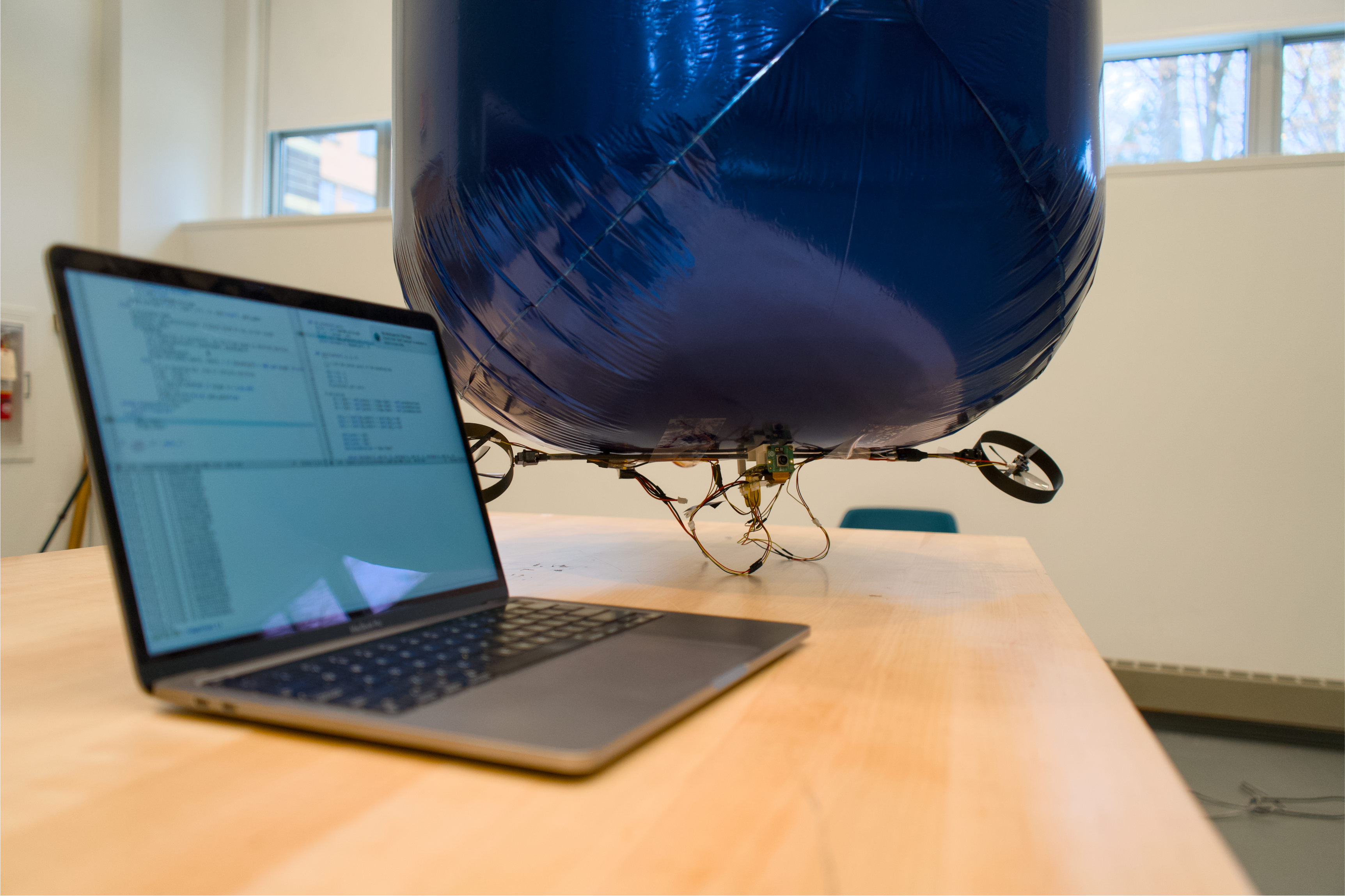 Robotic blimp indoors next to a laptop